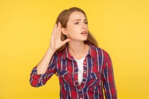 woman-holding-hand-to-ear-to-listen-on-yellow-background