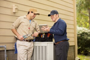 two-smiling-ac-technicians-standing-over-ac-outdoor-unit-looking-at-tablet