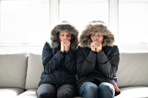 Couple bundled up in coats indoors, indicating need for heating system replacement.