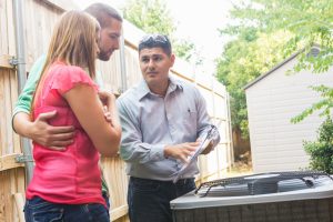 HVAC technician discussing cooling replacement options with a couple beside an outdoor AC unit.