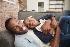 Father and son laughing together on a couch in a cool, comfortable home after cooling replacement.